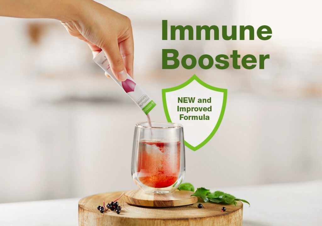 A hand pouring a sachet of Herbalife Immune Booster new and improved formula powder into a double-walled glass of water, placed on a wooden board with fresh elderberries.