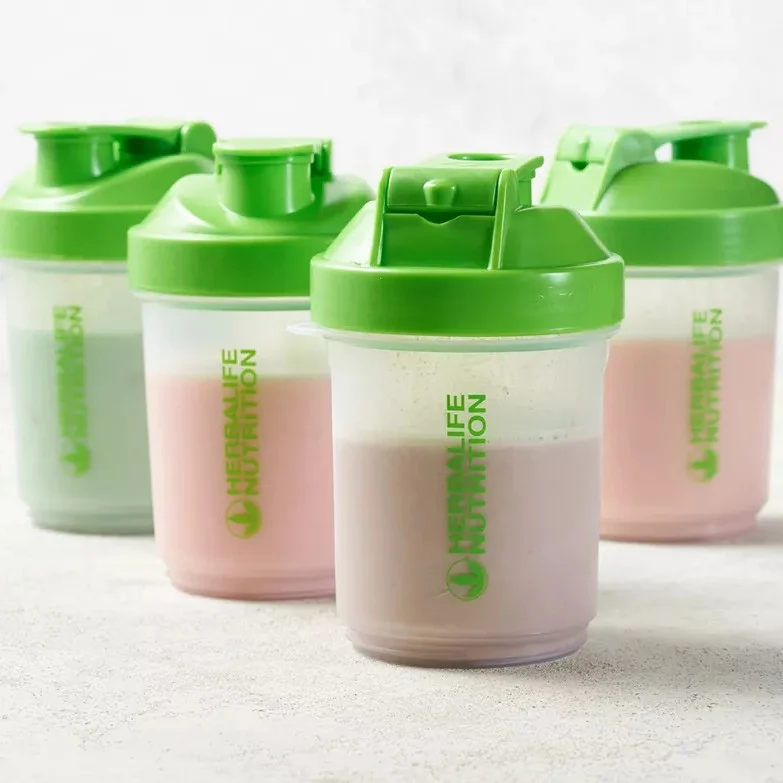 A row of official green Herbalife Nutrition Super Shaker cups filled with different colourful protein shakes on a bright textured background.
