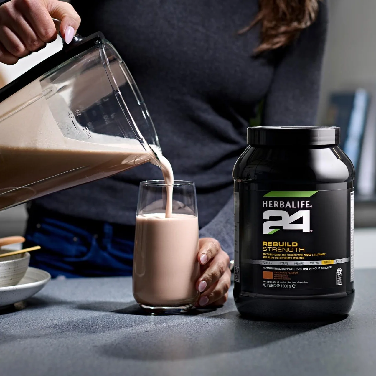 Herbalife24 Rebuild Strength chocolate recovery shake being poured from a blender jar into a glass on a modern kitchen counter