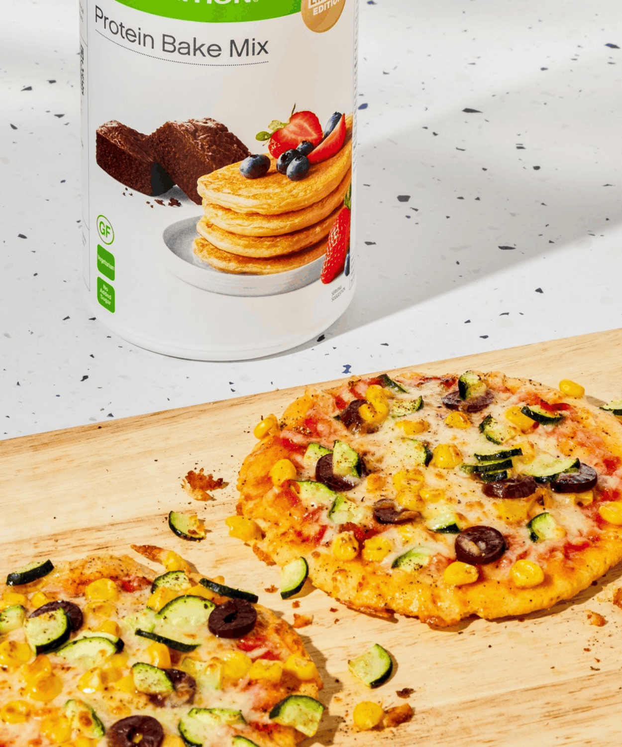 Two mini vegetable pizzas made with Herbalife Protein Bake Mix dough, topped with courgette, olives and sweetcorn, on a wooden board