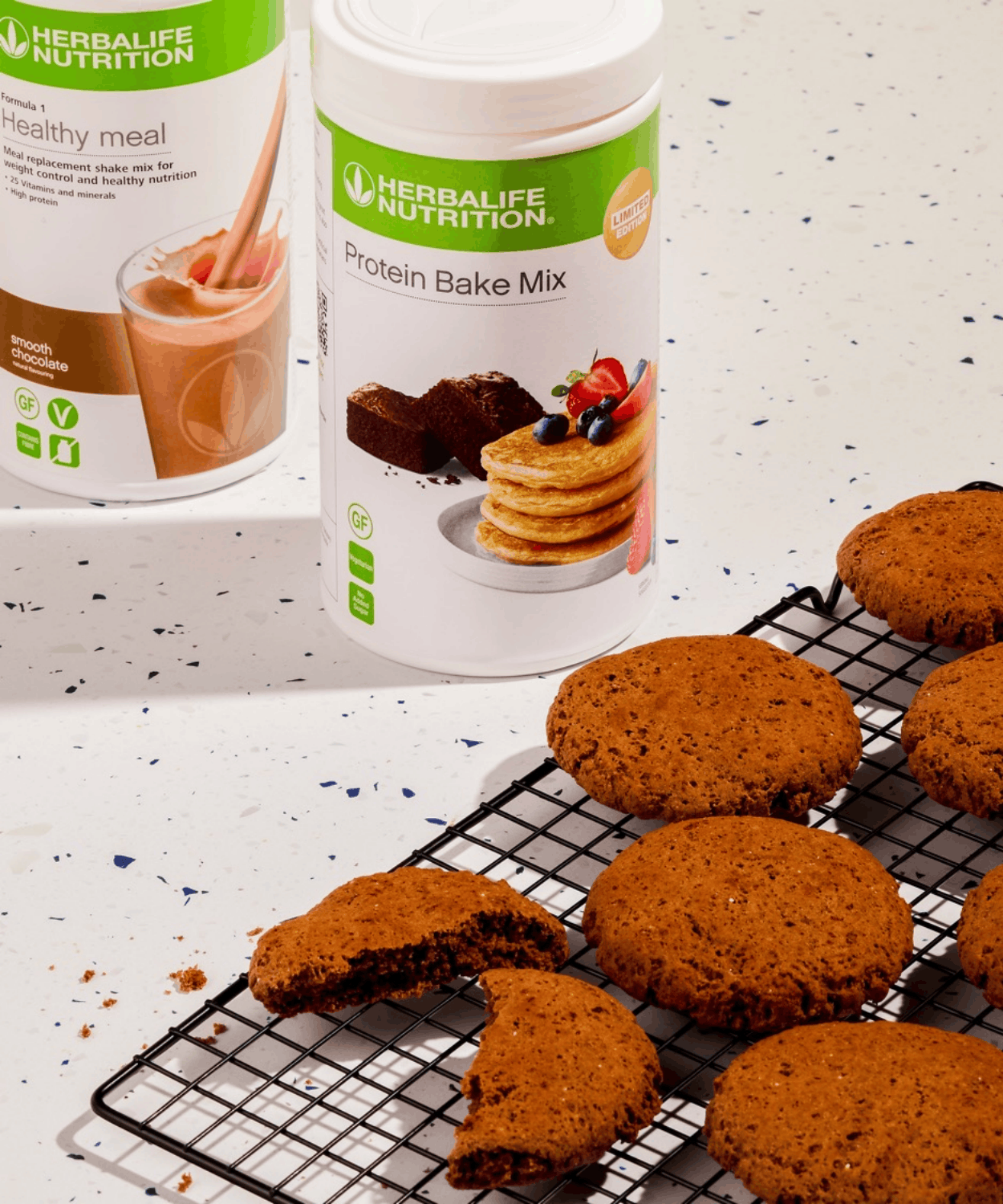Chocolate protein biscuits cooling on a wire rack beside Formula 1 Healthy Meal Smooth Chocolate and Protein Bake Mix tubs