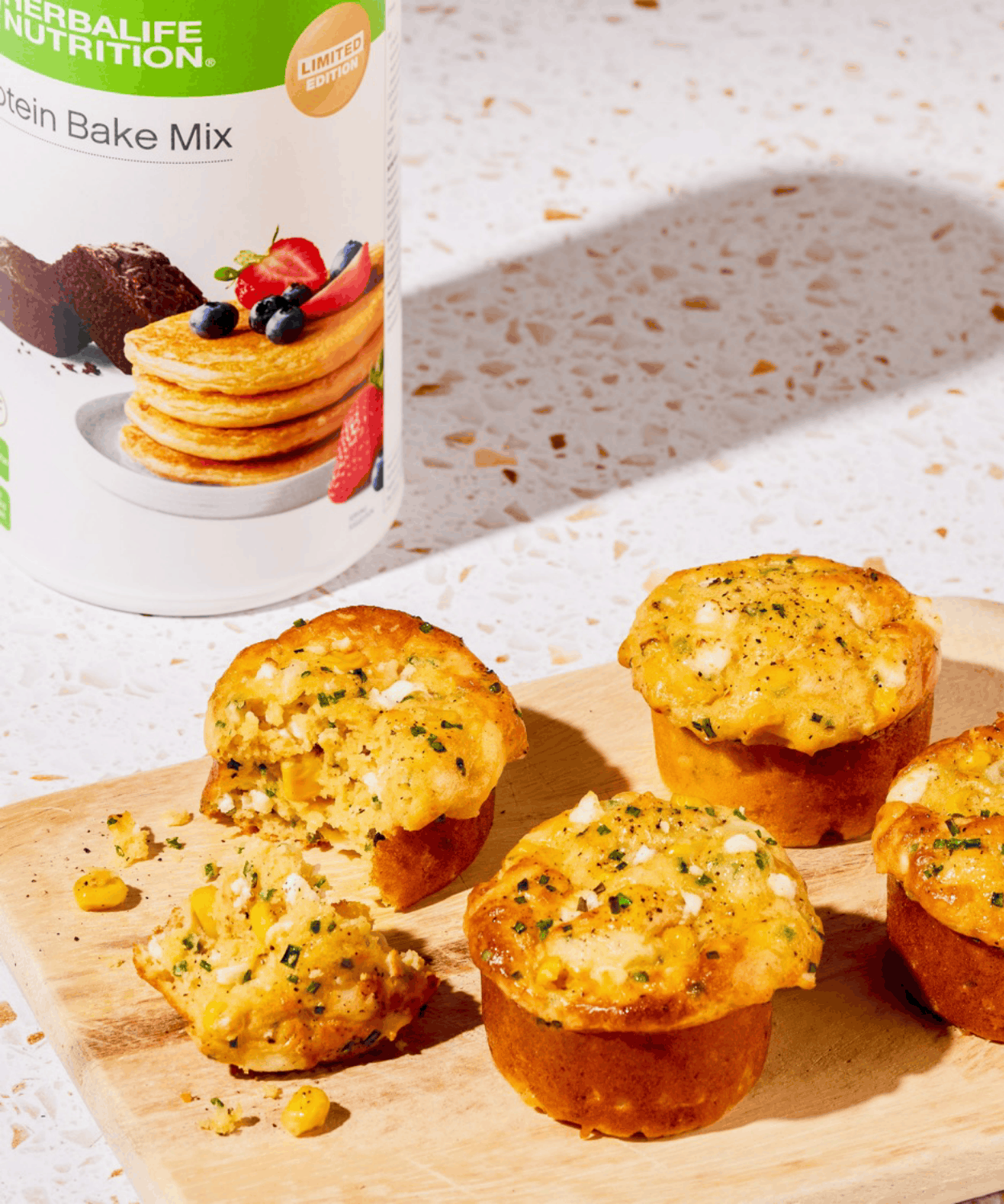Savoury protein muffins with sweetcorn and herbs on a wooden board beside the Herbalife Protein Bake Mix tub